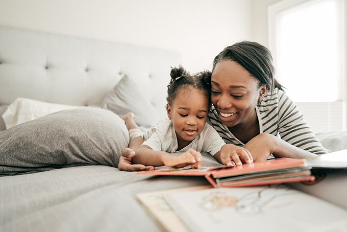 Black mother smiling and reading with her daughter in bed.