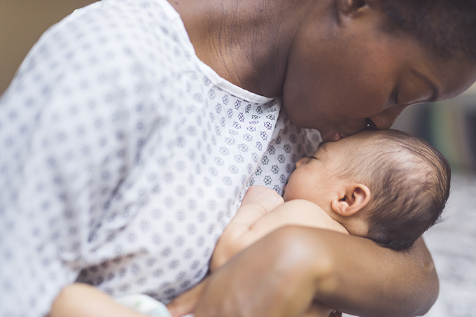Black mother in a hospital gown, kissing her baby.