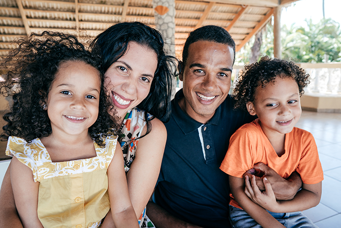 Multiracial family of four, smiling outdoors.