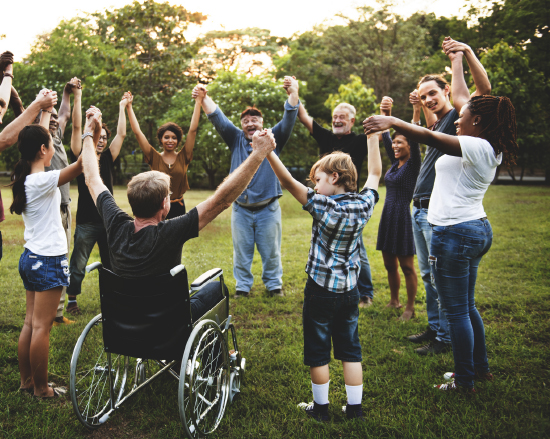 Diverse group of people forming a circle outside, holding hands together.